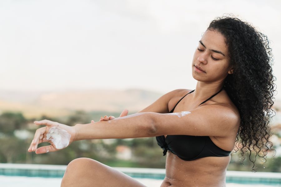 Woman with dark skin and long curly hair applying sunscreen to arms